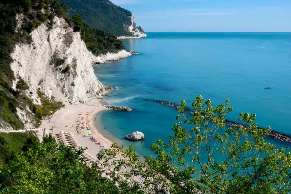 Spiaggia dei frati con scogliere bianche, mare azzurro e alberi verdi.