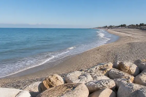 Spiaggia di Porto Sant'Elpidio Mare con rocce in primo piano e mare calmo sotto un cielo azzurro.