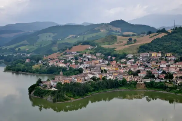 Borgo pittoresco affacciato su un lago, con case colorate e colline verdi sullo sfondo. Un gioiello nascosto nella regione di Urbino.