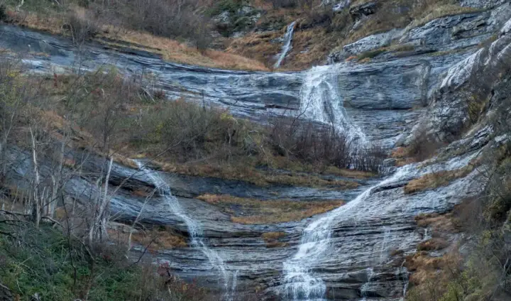 Le cascate della Volpara scendono su rocce stratificate, con vegetazione autunnale e alberi spogli che incorniciano il paesaggio.